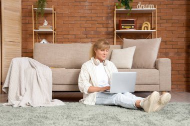 Evde dizüstü bilgisayar kullanan olgun bir kadın.