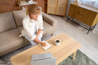 Evdeki masada dizüstü bilgisayarda yazan olgun bir kadın.