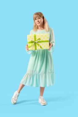 Mavi arka planda hediye kutusu olan güzel, olgun bir kadın.