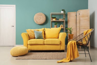 Şık oturma odasının içinde sarı kanepe, koltuk ve katlanır ekran var.