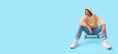 Kaykayın üzerinde oturan genç adam mavi arkaplan ve metin için boşluk var