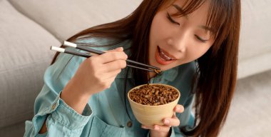 Yemek çubuklarıyla evde kızarmış böcek yiyen genç Asyalı kadın, yakın plan.