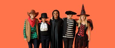 Farklı Cadılar Bayramı kostümleriyle turuncu arka planda mutlu çocuklar.