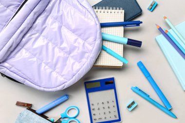 Gri arka planda farklı kırtasiye malzemeleriyle süslü okul çantası.