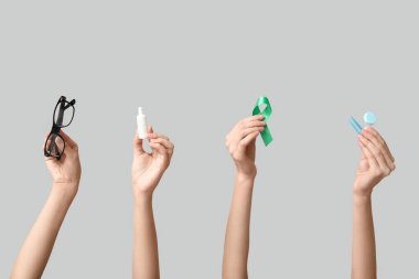 Göz damlası, cımbız, kontak lensler için kap yeşil kurdele ve gri arka planda gözlük takan kadın elleri. Glaucoma farkındalık kavramı