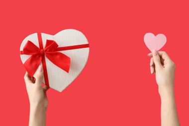 Kağıt kalpli kadın eller ve kırmızı arka planda hediye kutusu. Sevgililer Günü kutlaması