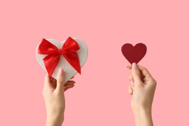 Kağıt kalpli kadın eller ve pembe arka planda hediye kutusu. Sevgililer Günü kutlaması