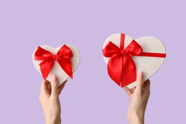 Leylak arka planında kalp şeklinde hediye kutuları olan kadın elleri. Sevgililer Günü kutlaması