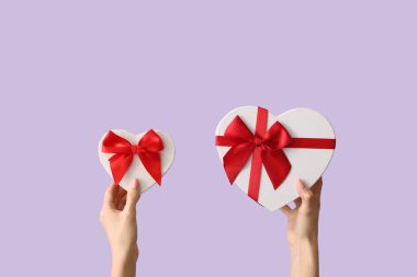 Leylak arka planında kalp şeklinde hediye kutuları olan kadın elleri. Sevgililer Günü kutlaması