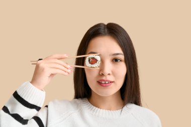 Güzel Asyalı bir kadın bir gözünü lezzetli suşi çubuklarıyla kaplıyor. Bej arka planda, yakın planda.