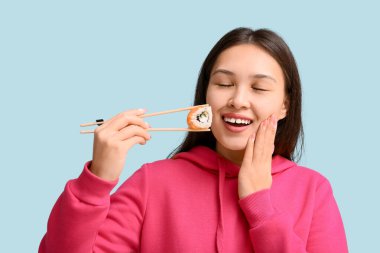 Rüyamda genç Asyalı bir kadın elinde lezzetli suşilerle mavi arka planda yemek çubukları tutuyor.