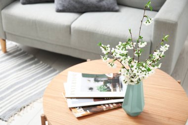 Şık oturma odasındaki masanın üzerinde çiçek açan dalları olan mavi vazo.