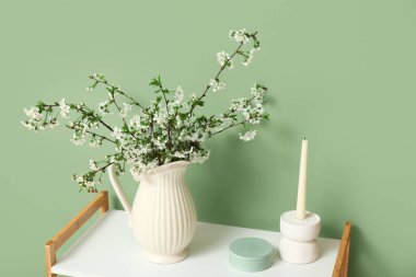 Çiçek açan dalları ve yeşil duvarın yanındaki masada mumu olan vazo.