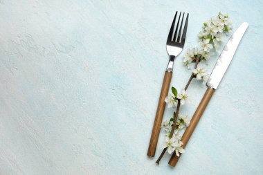 Açık mavi arkaplanda çiçek açan dallı gümüş çatal bıçak seti