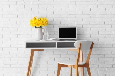 Oturma odasında dizüstü bilgisayarla sürahide nergis çiçekleri