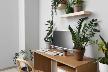 Workplace with computer and green houseplants in light office
