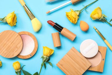 Mavi arka planda çiçekler, makyaj süngeri ve dekoratif kozmetik ürünleri olan güzel bir kompozisyon, yakın plan.