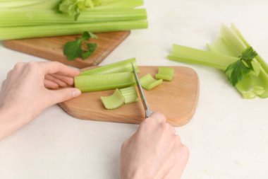 Beyaz arka planda taze yeşil kereviz kesen kadın.