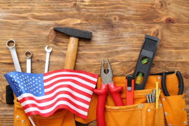 Farklı aletlere sahip kemer ve ahşap arka planda Amerikan bayrağı. İşçi Bayramı kutlamaları