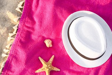 Şık hasır şapkalı renkli havlu, deniz kabuğu ve kumdaki deniz yıldızı, yakın plan.