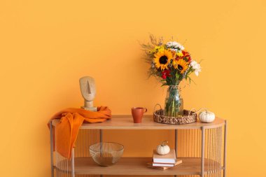 Sonbahar çiçekleri, balkabakları ve turuncu duvarın yanında dekoru olan ahşap raf ünitesi.