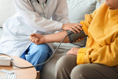 Doktor evde yaşlı bir kadının kan basıncını ölçüyor.