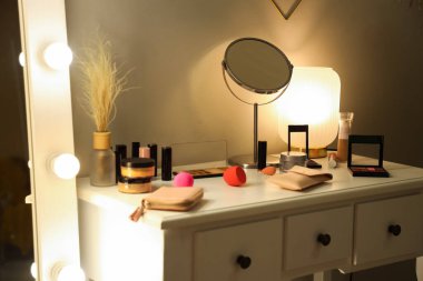 Dressing table with decorative cosmetics, mirror and glowing lamp in dark makeup room