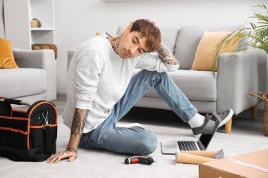 Düşünceli genç adam evde mobilya montajı yapıyor.