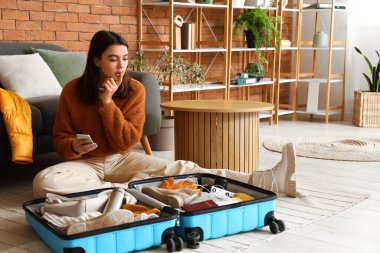 Cep telefonlu genç bir kadın kışlık kıyafetlerini bavuluna koyup eve gidiyor.