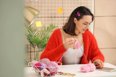 Evde iğnelerle örgü ören genç bir kadın.