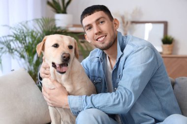 Labrador köpeği olan genç adam evdeki kanepede oturuyor.