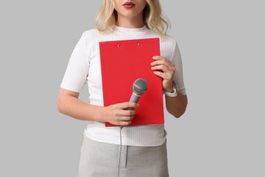 Gri arka planda mikrofonu ve panosu olan kadın gazeteci, yakın plan