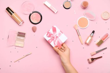 Hediye kutusu ve pembe arka planda farklı makyaj ürünleri olan bir kadın.