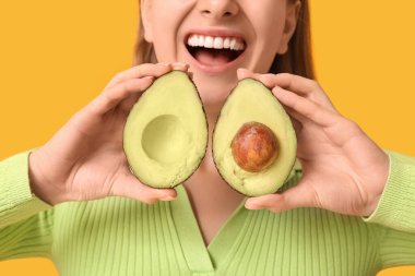 Sarı arka planda avokadosu olan genç bir kadın, yakın plan.