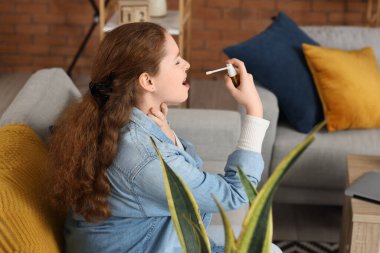 Evde tıbbi sprey kullanan boğazı ağrıyan hasta genç bir kadın.