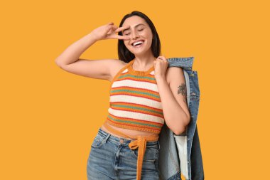 Sarı arka planda şık kot elbiseli güzel, genç ve mutlu bir kadın.