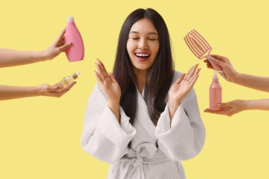 Bornozlu genç Asyalı kadın ve sarı arka planda saç ürünleri olan eller.