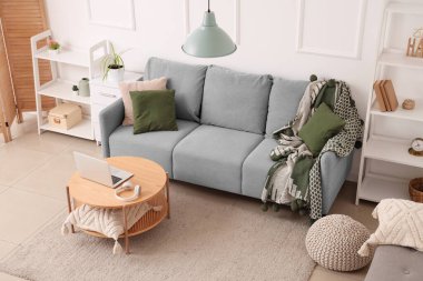 Modern interior of living room with grey sofa and laptop on table