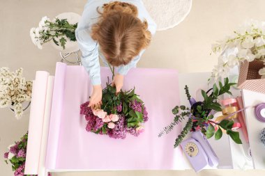 Kadın çiçekçi dükkanda leylaklarla buket yapıyor.