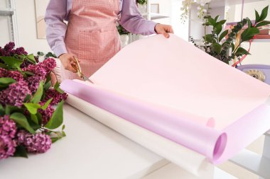 Çiçekçi kadın dükkanda buket için paket kağıdı kesiyor.