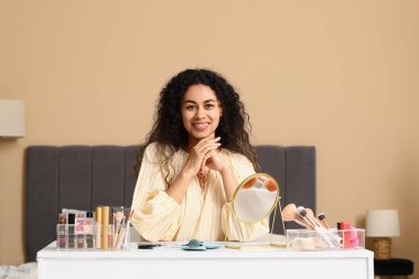 Güzel, genç, mutlu, kozmetik ürünleriyle evde makyaj yapan Afro-Amerikan kadın.