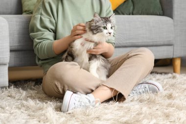 Uzun saçlı tatlı kedisi olan genç bir kadın oturma odasında yerde oturuyor.
