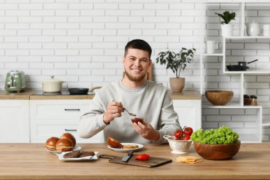 Genç adam mutfakta lezzetli bir burger için ekmeğe ketçap koyuyor.