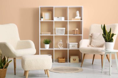 Bej duvarın yanında raflar ve koltuklar