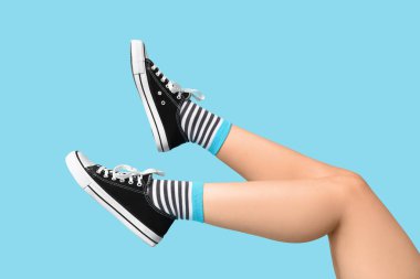 Çoraplı genç kadın bacakları ve mavi arka planda siyah spor ayakkabılar.