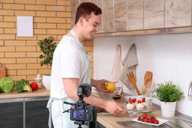 Tatlı kekleri ve taze çilekleri olan genç bir adam mutfakta yemek videosu kaydediyor.