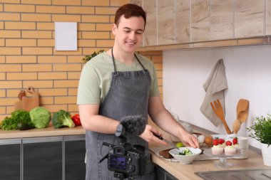 Tatlı kekleri olan genç adam mutfakta yemek pişirme videosu kaydediyor.