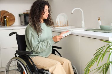 Tekerlekli sandalyedeki genç Afro-Amerikalı kadın evde bulaşık yıkıyor.