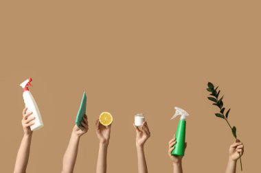 Deterjan şişeleri, paçavra, yeşil dal, limon ve kavanoz taşıyan kahverengi arka planda temizlik maddesi olan kadın elleri.