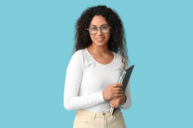 Mavi arka planda not defterleri olan Afro-Amerikalı genç bir iş kadını.